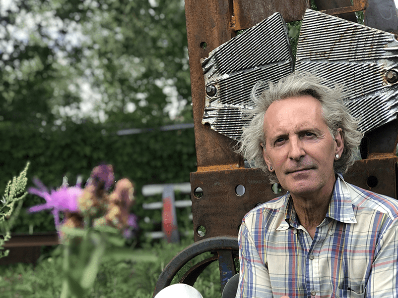 Glen LeMesurier qui se tient devant une de ses oeuvre en fer recyclé