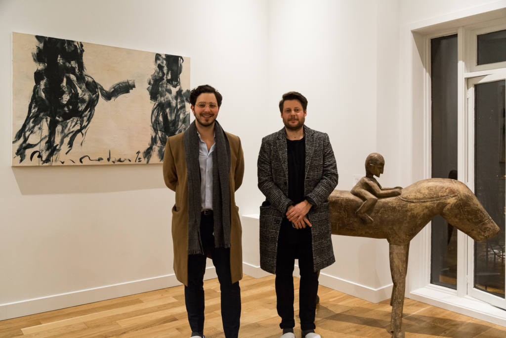 Deux hommes posent devant une sculpture en bois dans un appartement